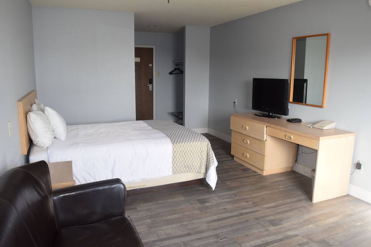 A bedroom with a bed, a desk, a chair, a television, and a mirror.