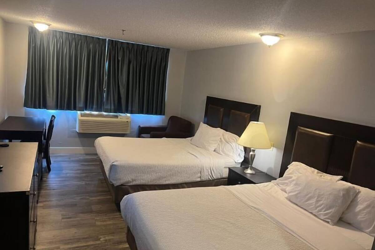 A hotel room with two beds, a desk, a chair, and a window with curtains.