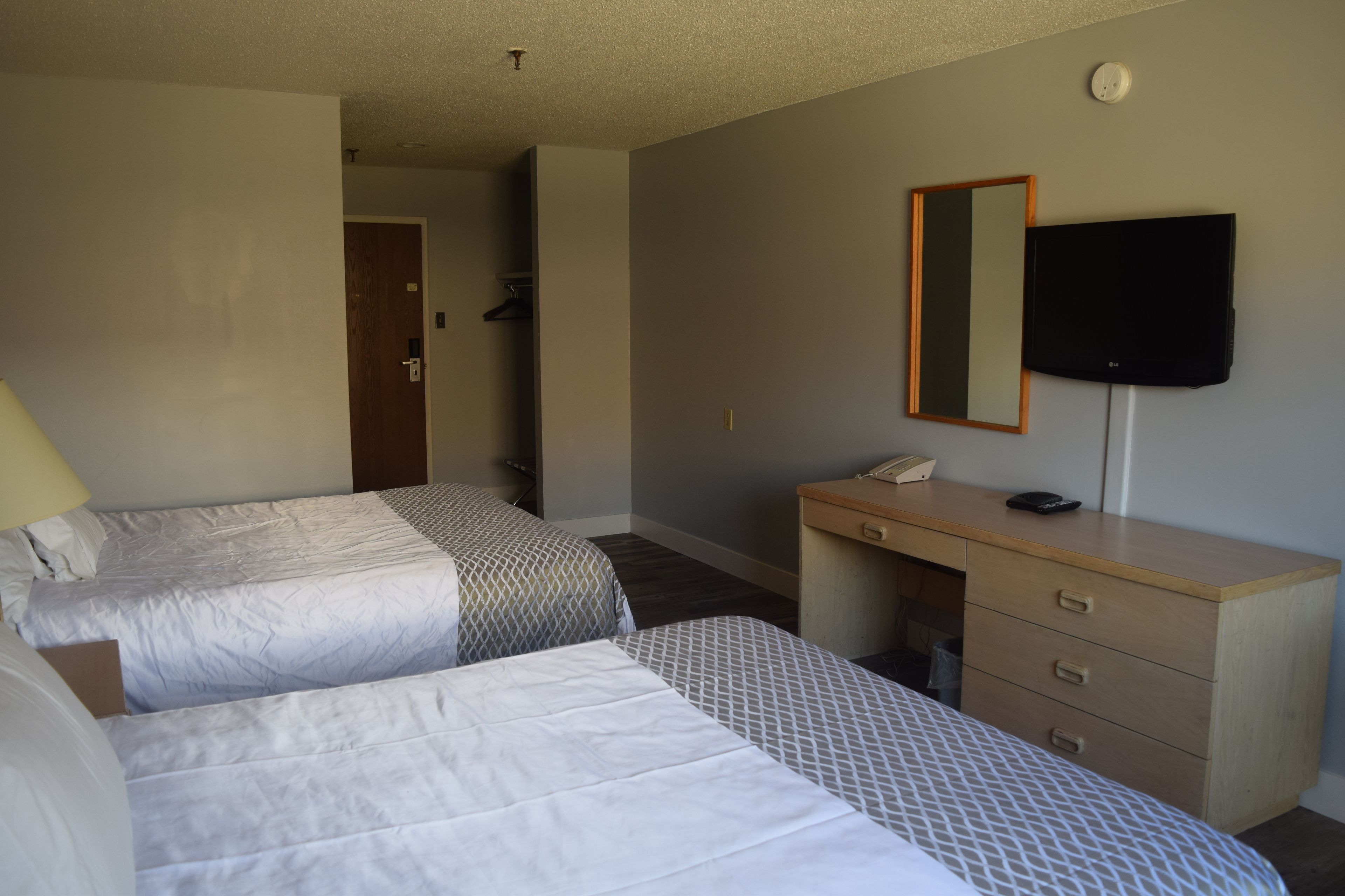 Habitación de hotel con dos camas, un escritorio, una silla, un televisor de pantalla plana y un espejo.
