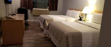 A hotel room with two beds, a desk, a television, and a window with curtains.