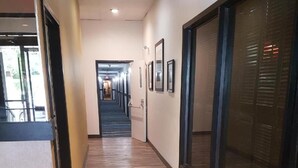 Un pasillo con suelo de madera, cuadros en las paredes y una puerta de cristal a la derecha.