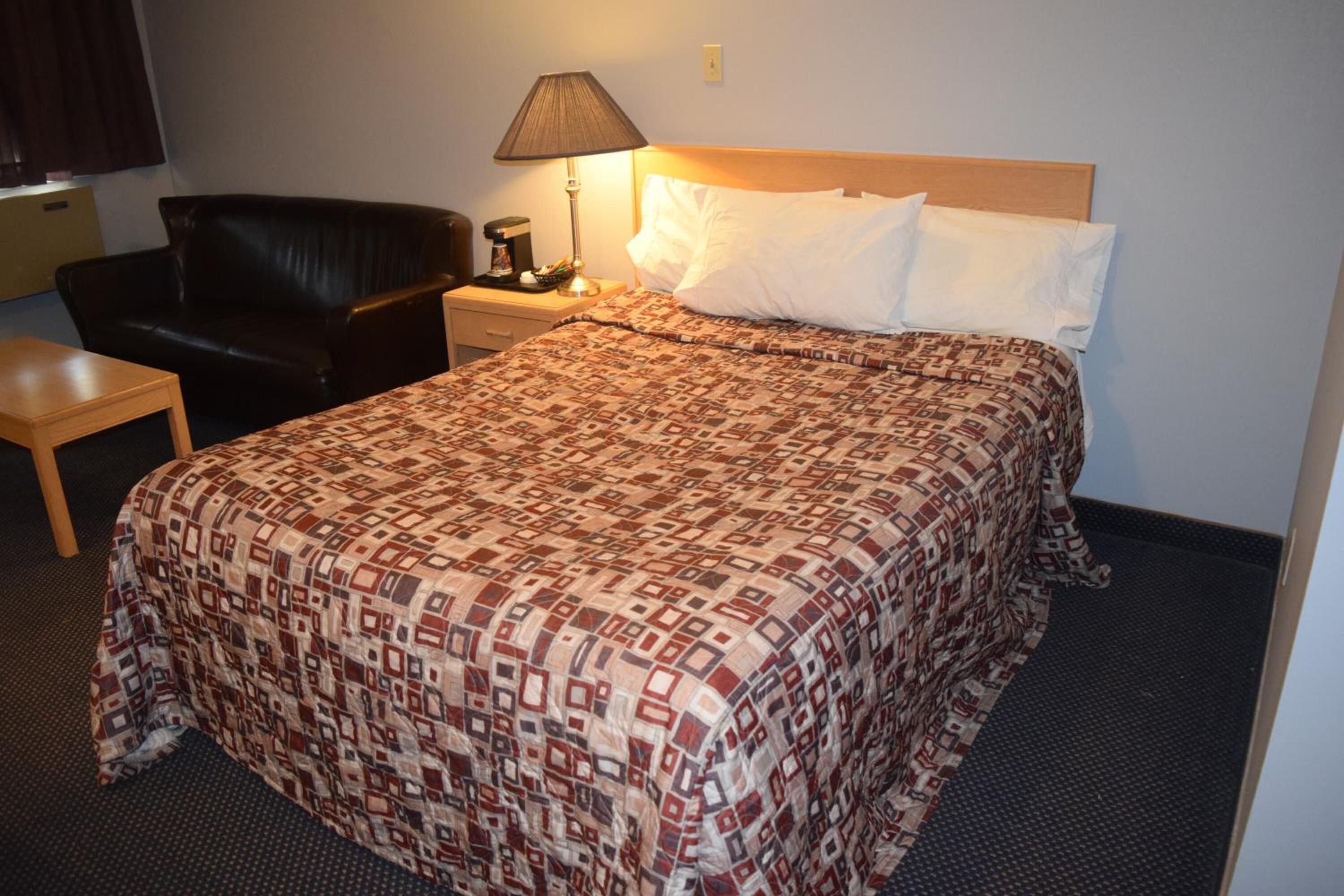 A hotel room with a bed, a nightstand with a lamp, a chair, and a small table.