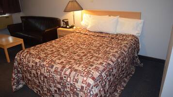 A hotel room with a bed, a nightstand with a lamp, a chair, and a small table.