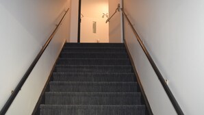 Una escalera con peldaños alfombrados y barandales de metal, que lleva a una puerta en la parte superior.