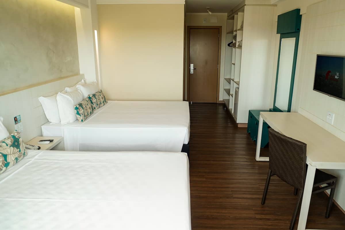 A hotel room with two beds, a desk, a chair, a TV, and a wardrobe.