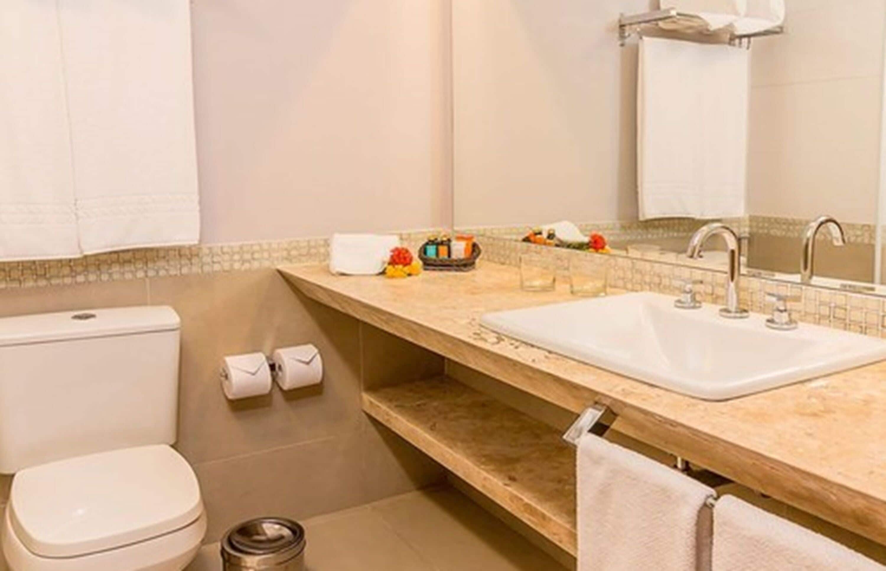 Une salle de bain avec des toilettes, un lavabo et un miroir. On y trouve des serviettes et des articles de toilette sur le comptoir.