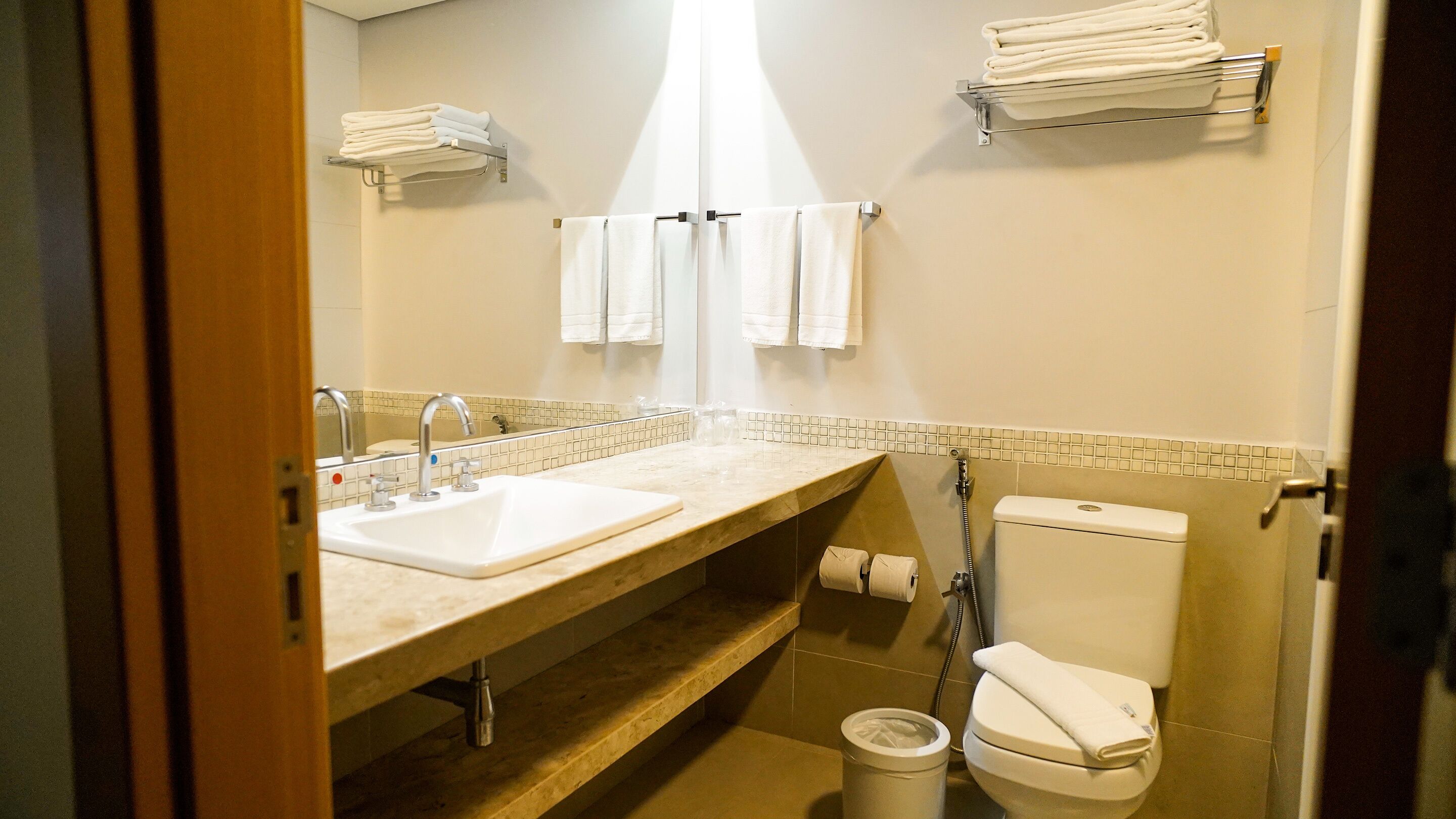 Un baño con lavamanos, dos llaves, inodoro y espejo.