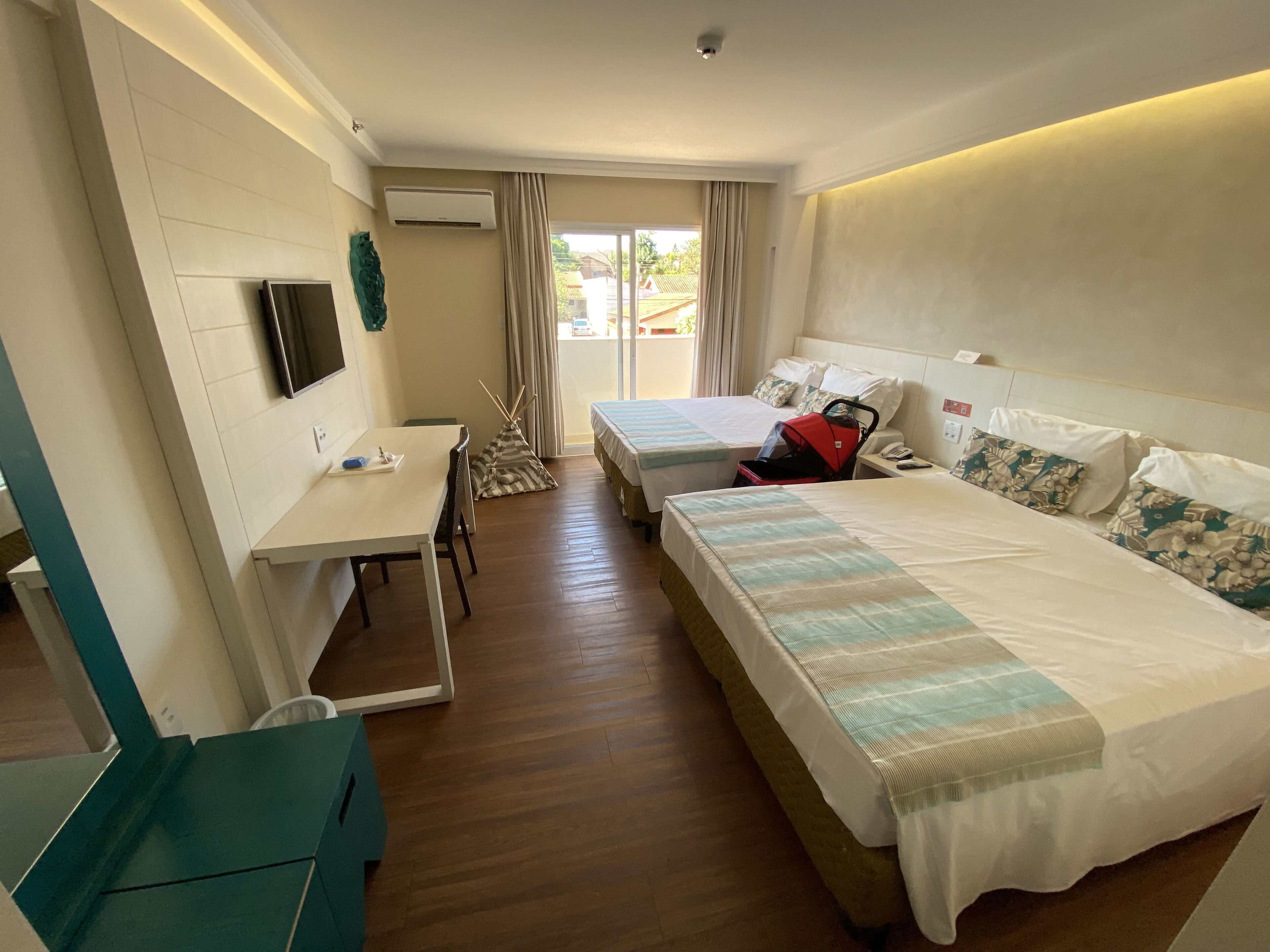 Une chambre d’hôtel avec deux lits, un bureau, une chaise, une télévision et une fenêtre avec des rideaux.