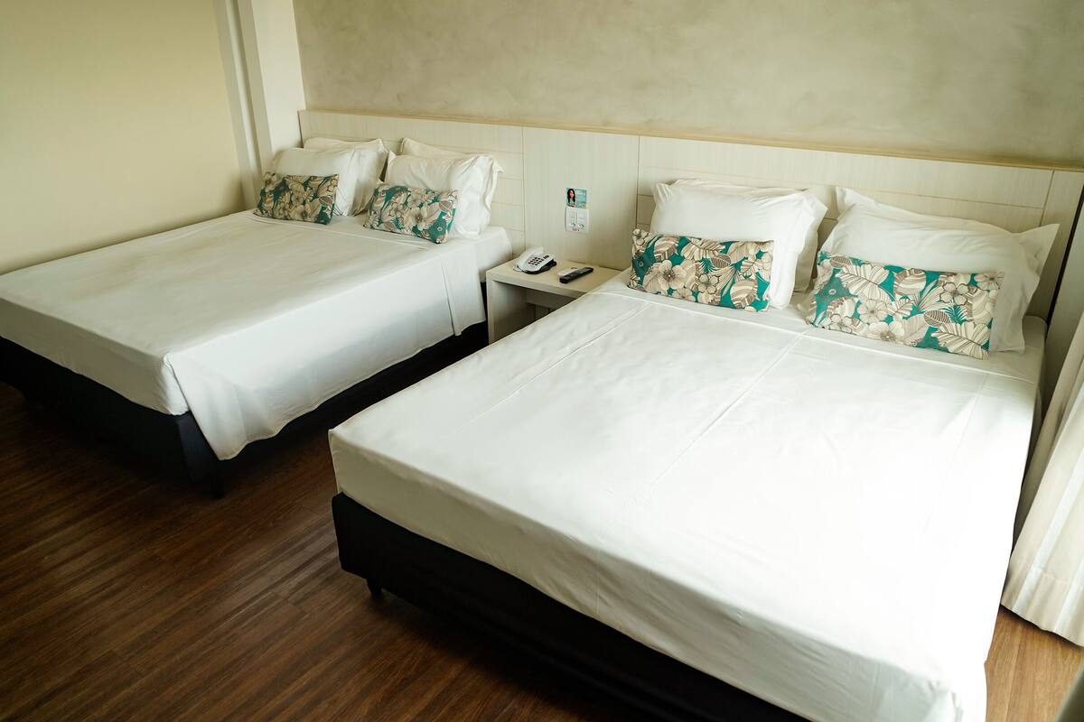 Two single beds with white linens and floral-patterned pillows, a bedside table with a phone and remote, and a wooden floor.