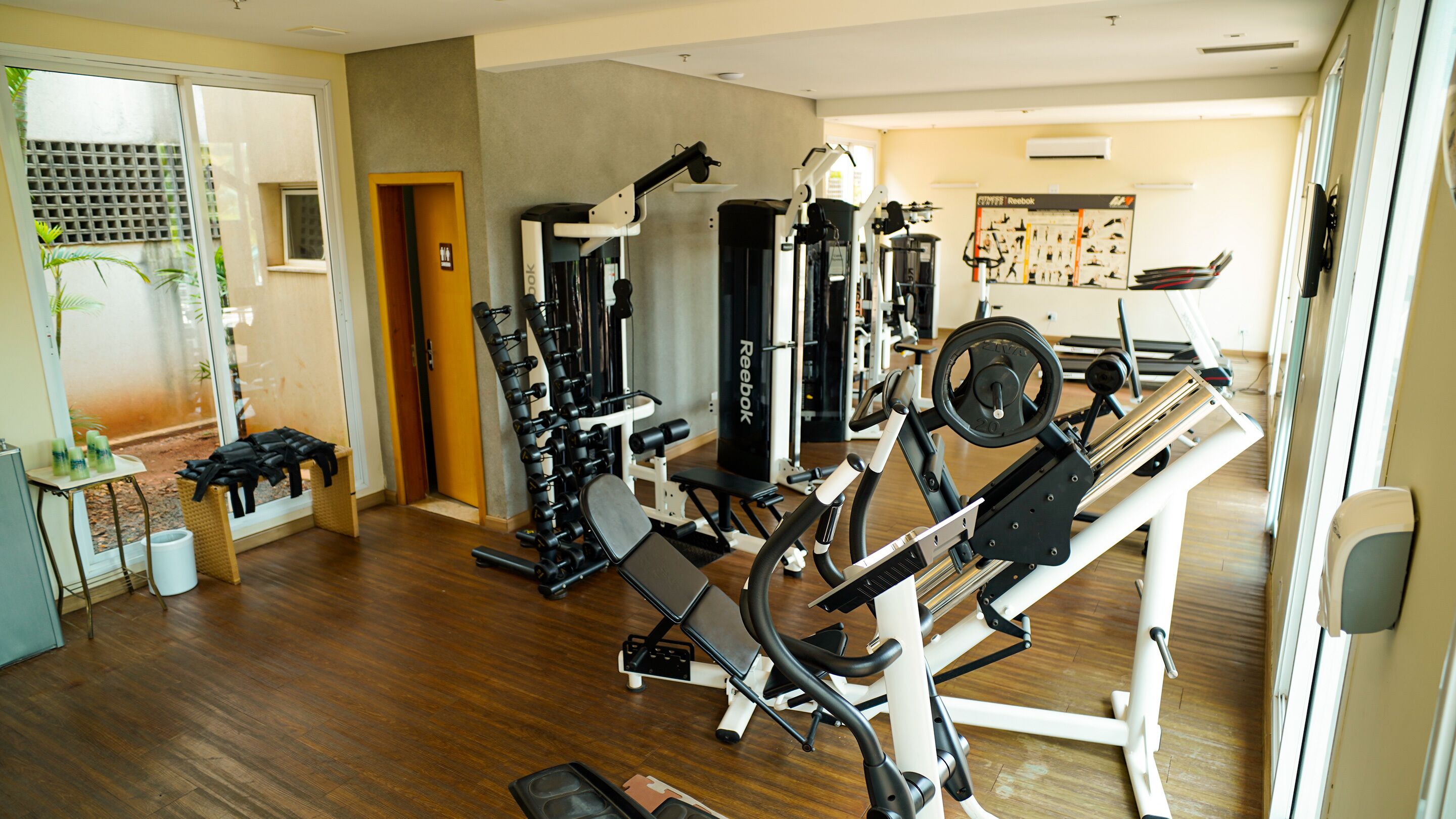 A gym with various exercise equipment, a wooden floor, and a wall with a Reebok poster.