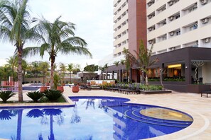 A hotel with a swimming pool, palm trees, and outdoor seating areas.