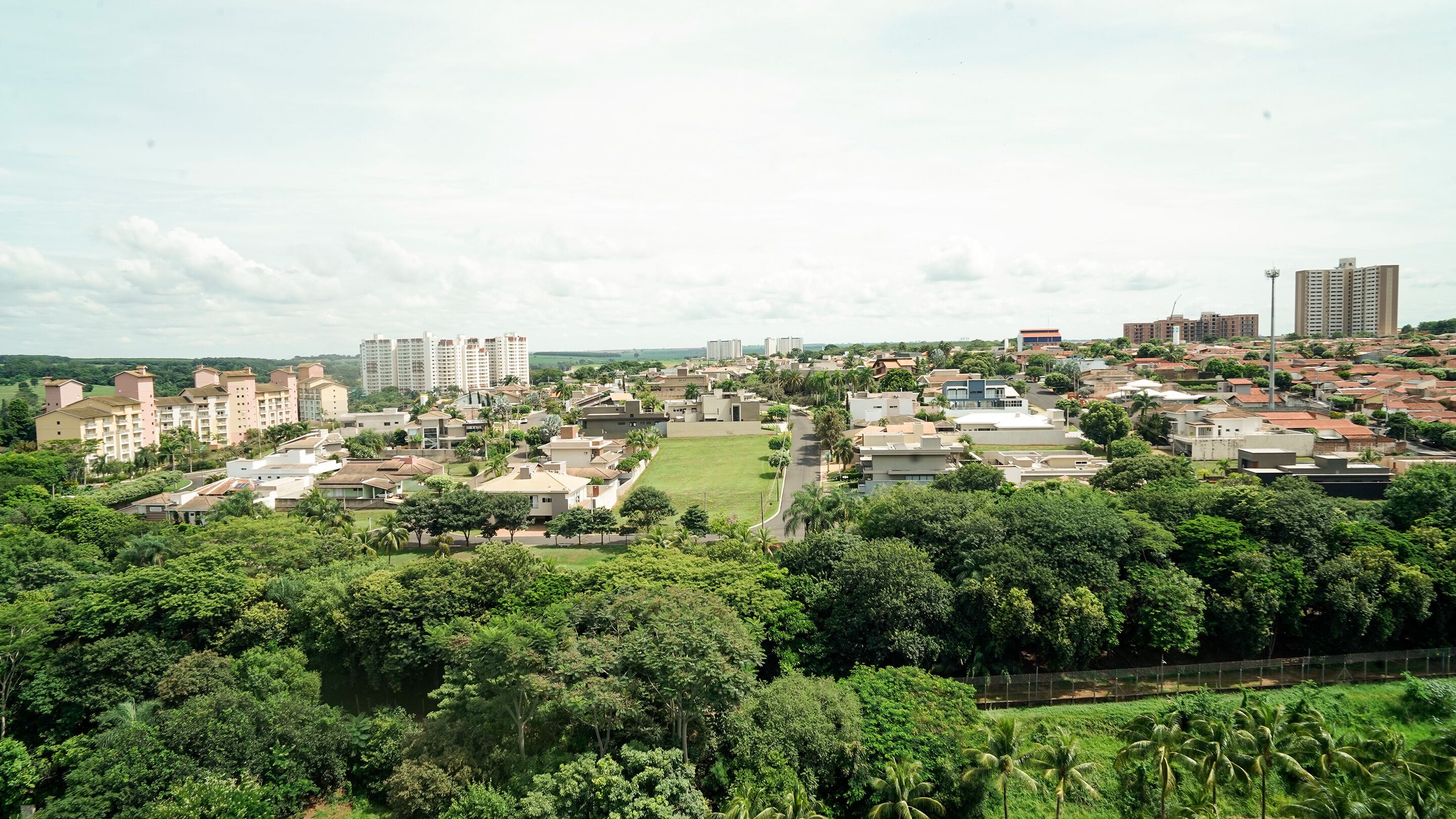 Zona residencial amb edificis de diverses alçades, tant de planta com alts, envoltada de vegetació i un cel serè.