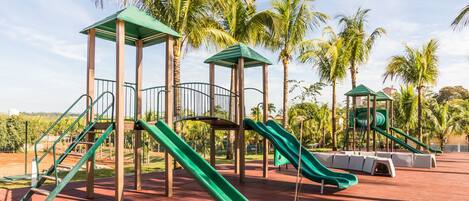 Un parque infantil con toboganes y estructuras de escalada, rodeado de palmeras.