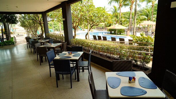 An outdoor dining area with tables and chairs, a pool, and palm trees in the background.