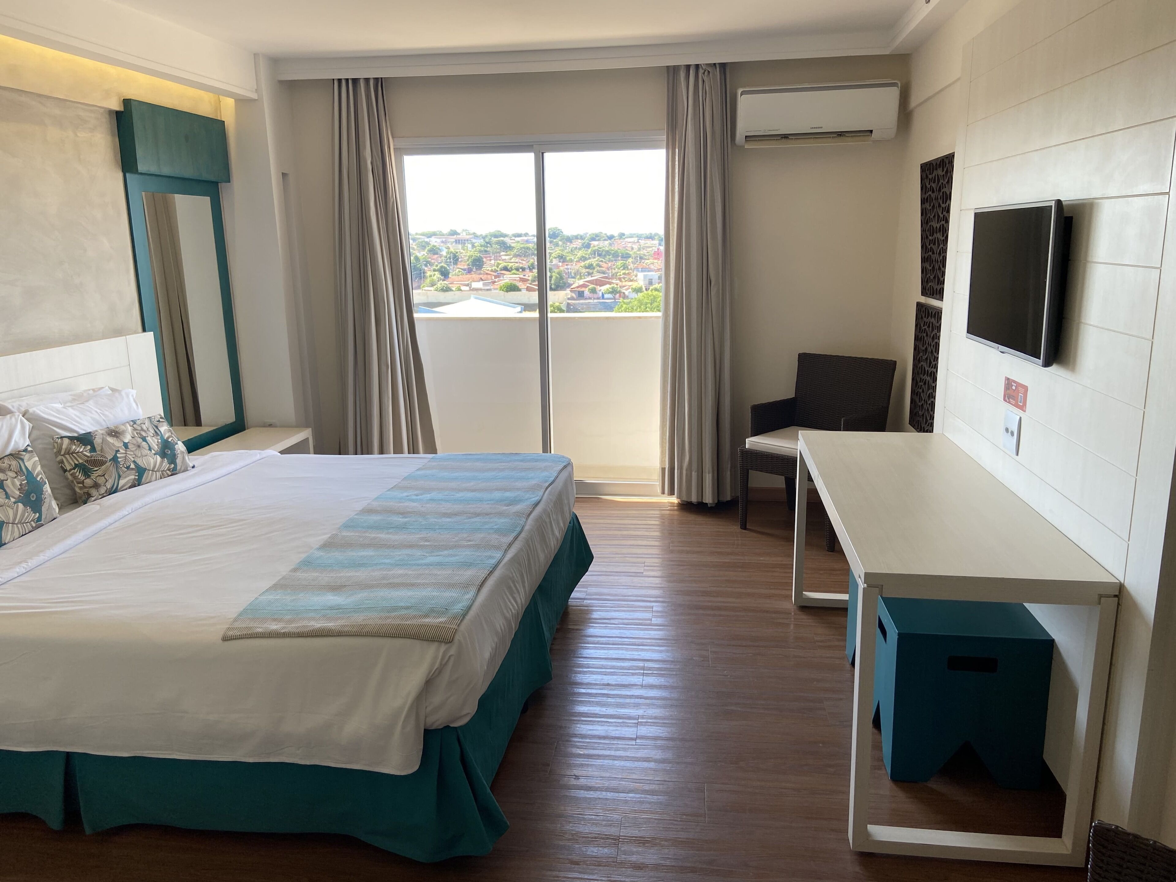 Hotelkamer met een bed, bureau, stoel, televisie en een balkon met uitzicht op de stad.