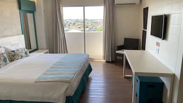 Habitación de hotel con cama, escritorio, silla, televisor y balcón con vista a la ciudad.