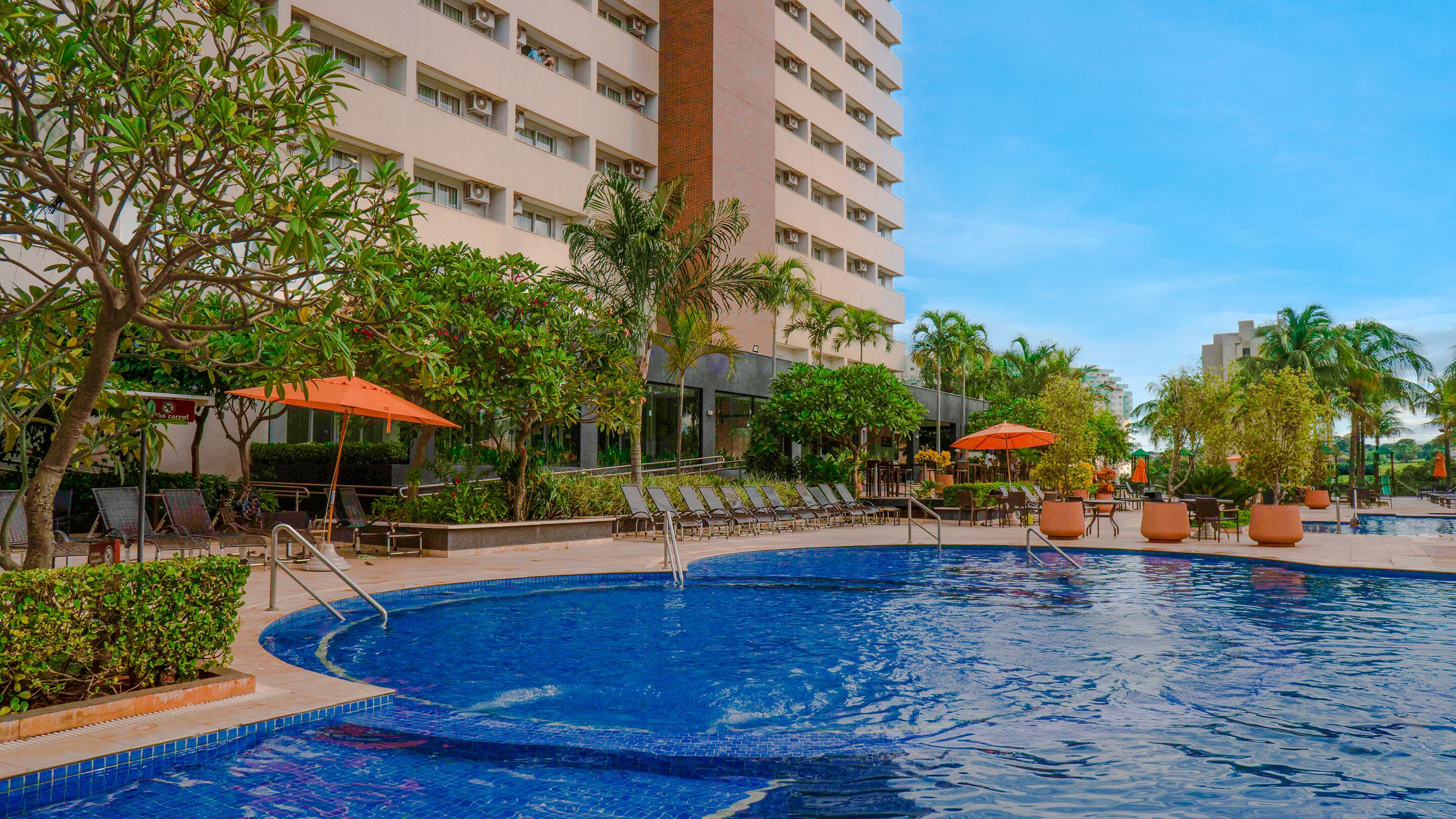 A hotel pool area with lounge chairs, umbrellas, and a large pool.