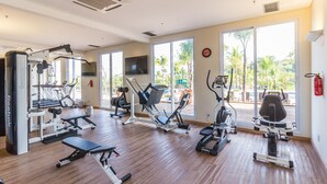 A gym with various exercise equipment, large windows, and a view of palm trees.
