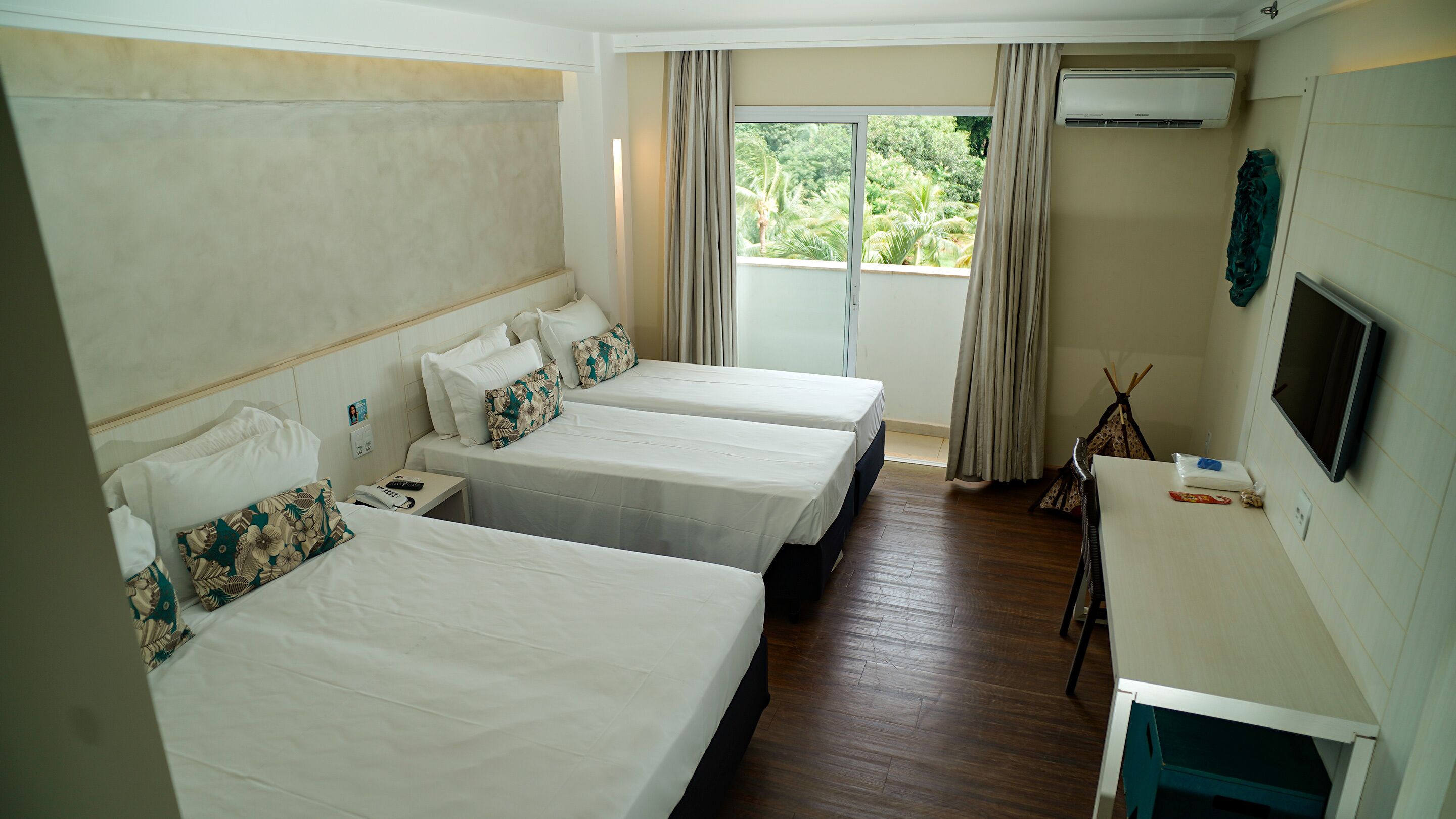 A hotel room with two beds, a desk, a TV, and an air conditioning unit.