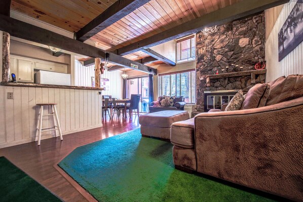 A cozy living room with a stone fireplace, wooden beams, and a plush sofa.