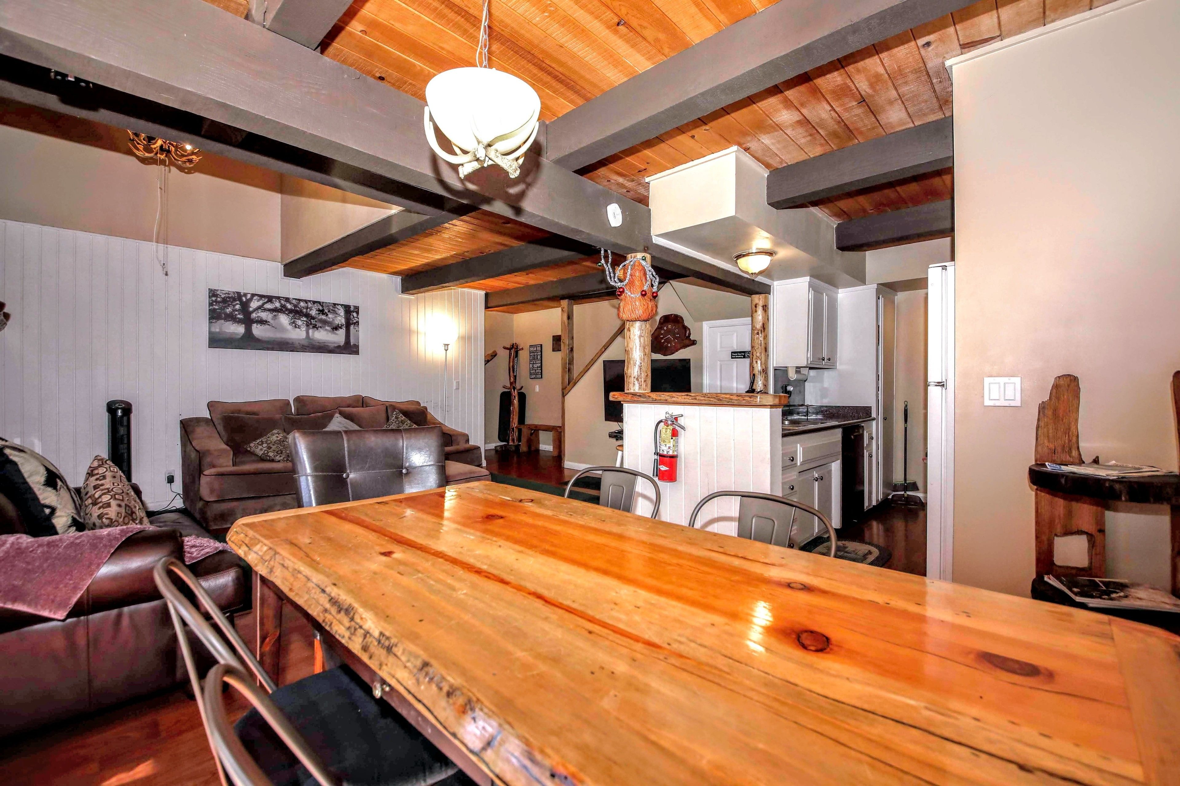 A spacious living room with a large wooden dining table, leather sofas, and a high ceiling with exposed beams.