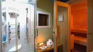 A sauna with a wooden interior, a glass-enclosed shower area with multiple showerheads, and a small table with towels and candles. - El Corral de Concilio (Murillo de Gallego)