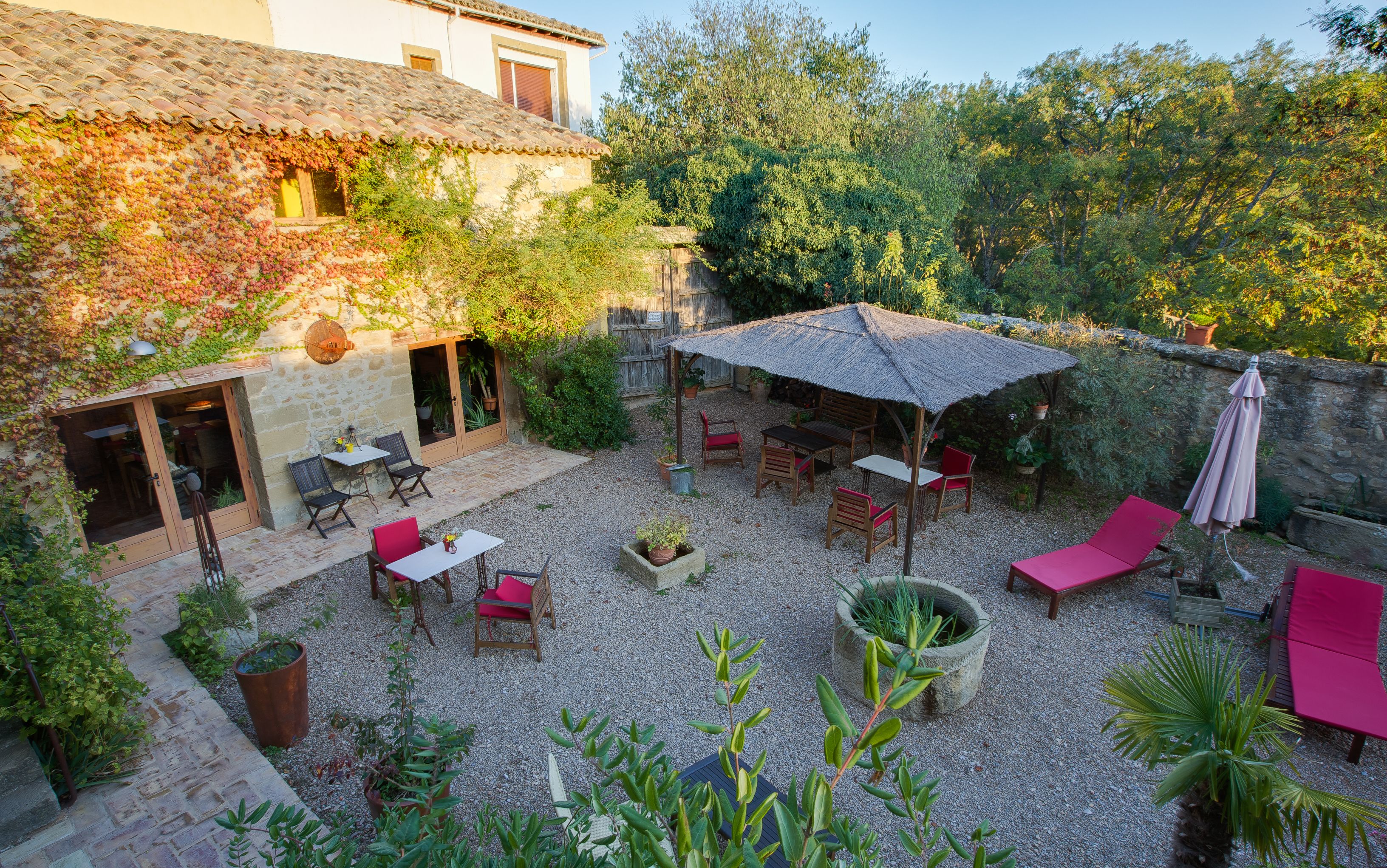 A courtyard with stone walls, a thatched-roof outdoor seating area, and potted plants.