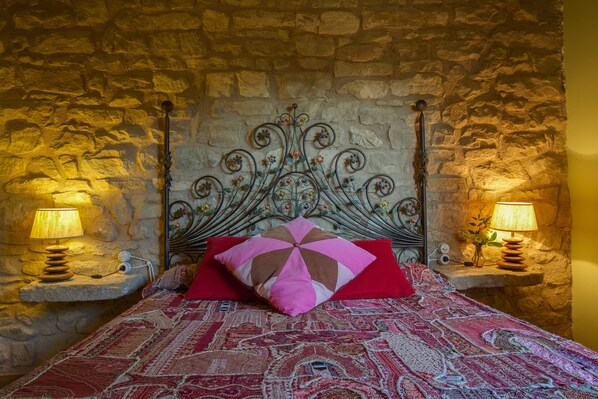 Ein Bett mit einem steinernen Kopfstück, zwei Nachttischlampen und einer gemusterten Bettdecke.