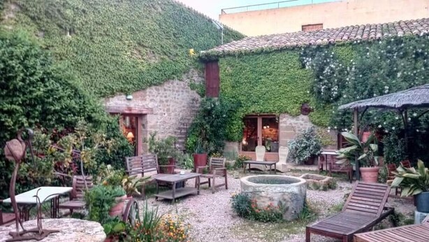 An outdoor patio with stone tables and chairs, surrounded by lush greenery and a stone wall. - El Corral de Concilio (Murillo de Gallego)