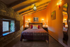 Ein Schlafzimmer mit einem großen Bett, Steinwänden, Holzbalken und zwei Nachttischlampen.