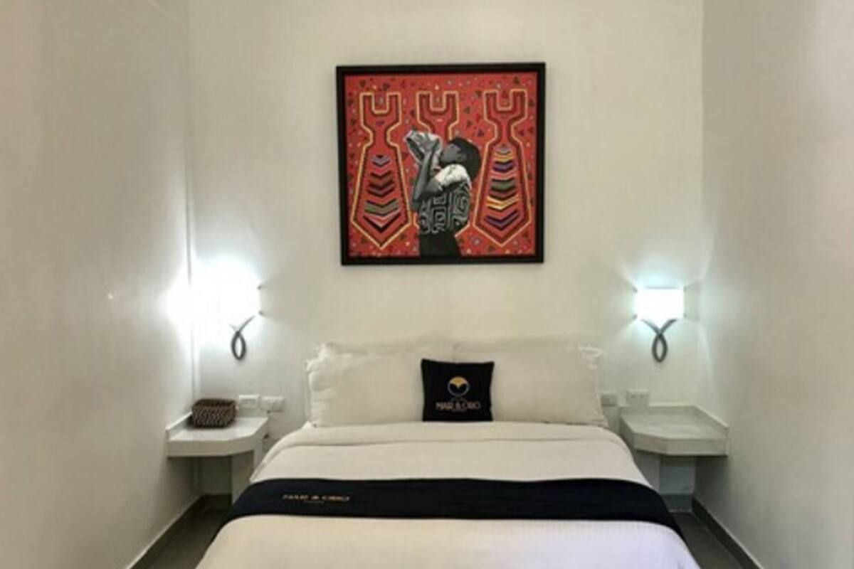A hotel room with a bed, white walls, a framed artwork above the bed, and two bedside tables with lamps.