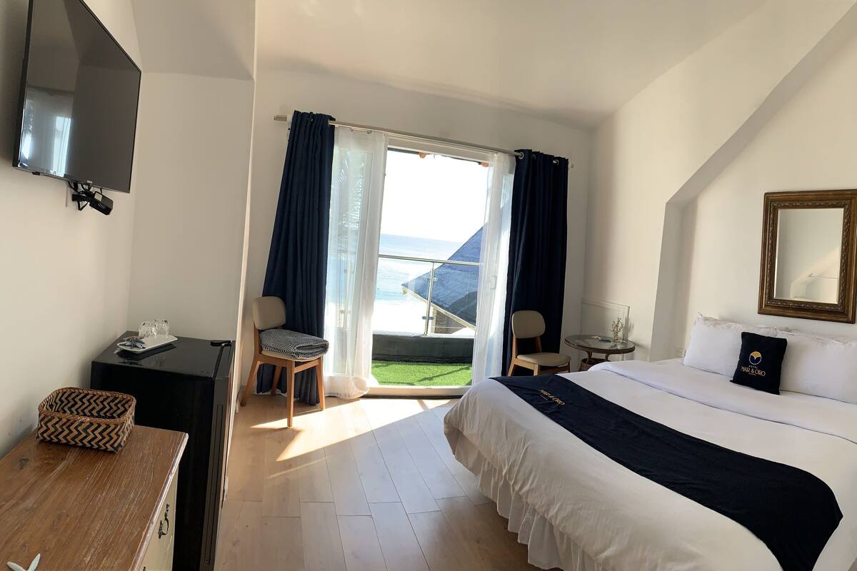 A hotel room with a bed, a TV, a desk, a chair, a small table, and a window with curtains.
