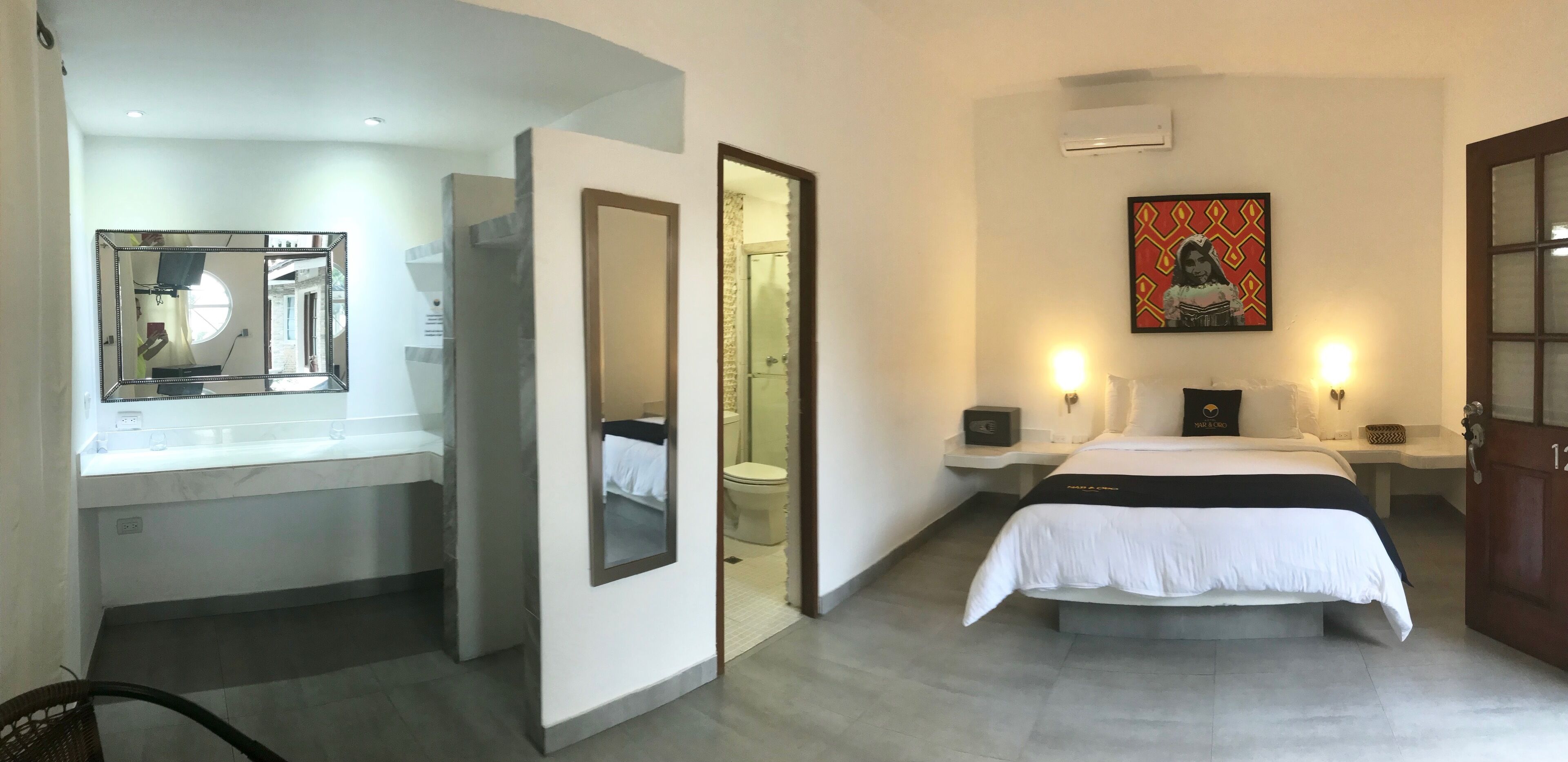 A hotel room with a bed, bedside tables, a mirror, a painting, and a door.