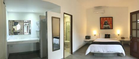 A hotel room with a bed, bedside tables, a mirror, a painting, and a door.