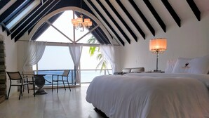 Une chambre d’hôtel avec un grand lit, un bureau avec une chaise, une lampe et une vue sur la mer.