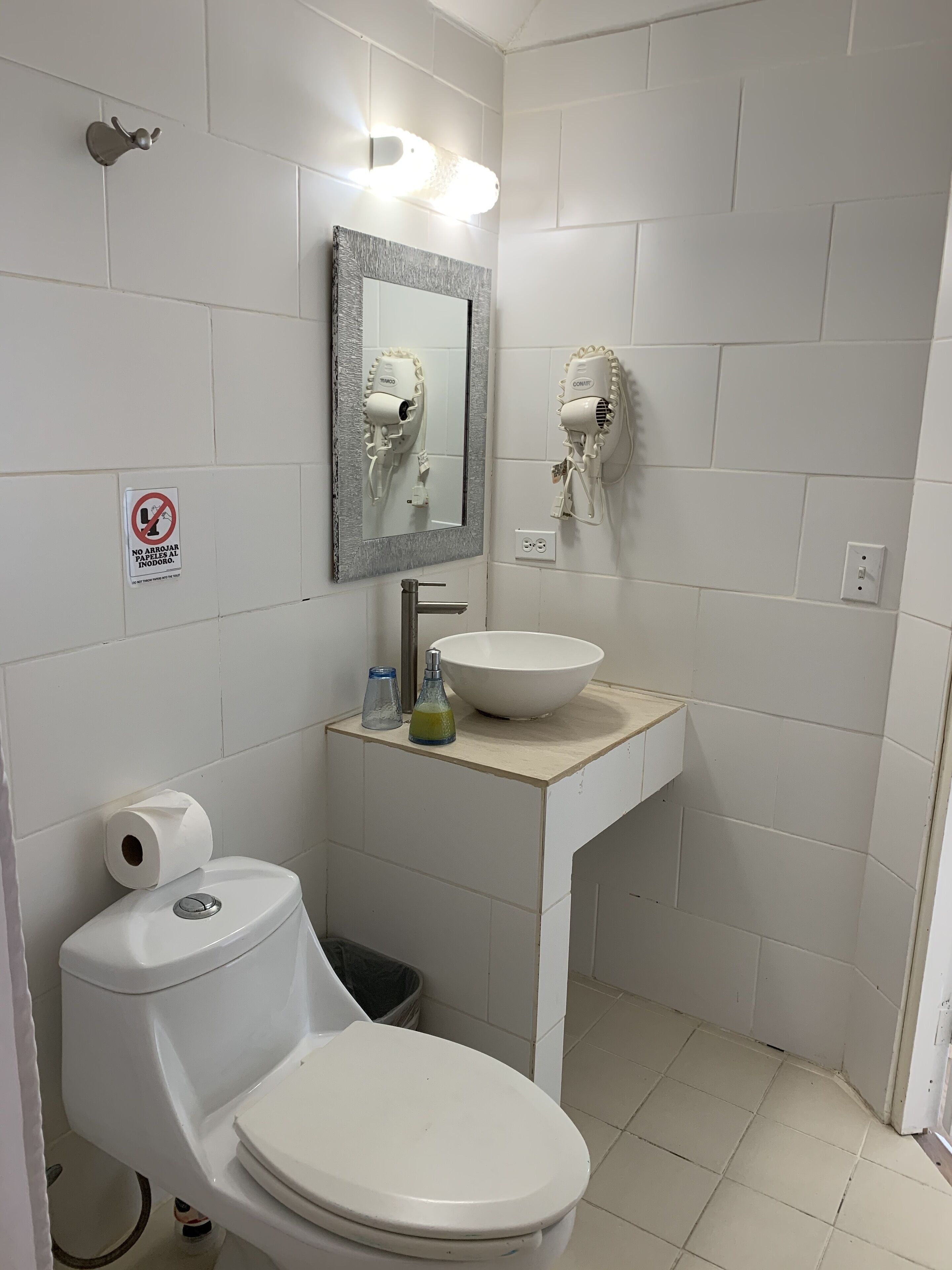 Un baño pequeño con inodoro, lavamanos y dos secadores de pelo fijados a la pared.