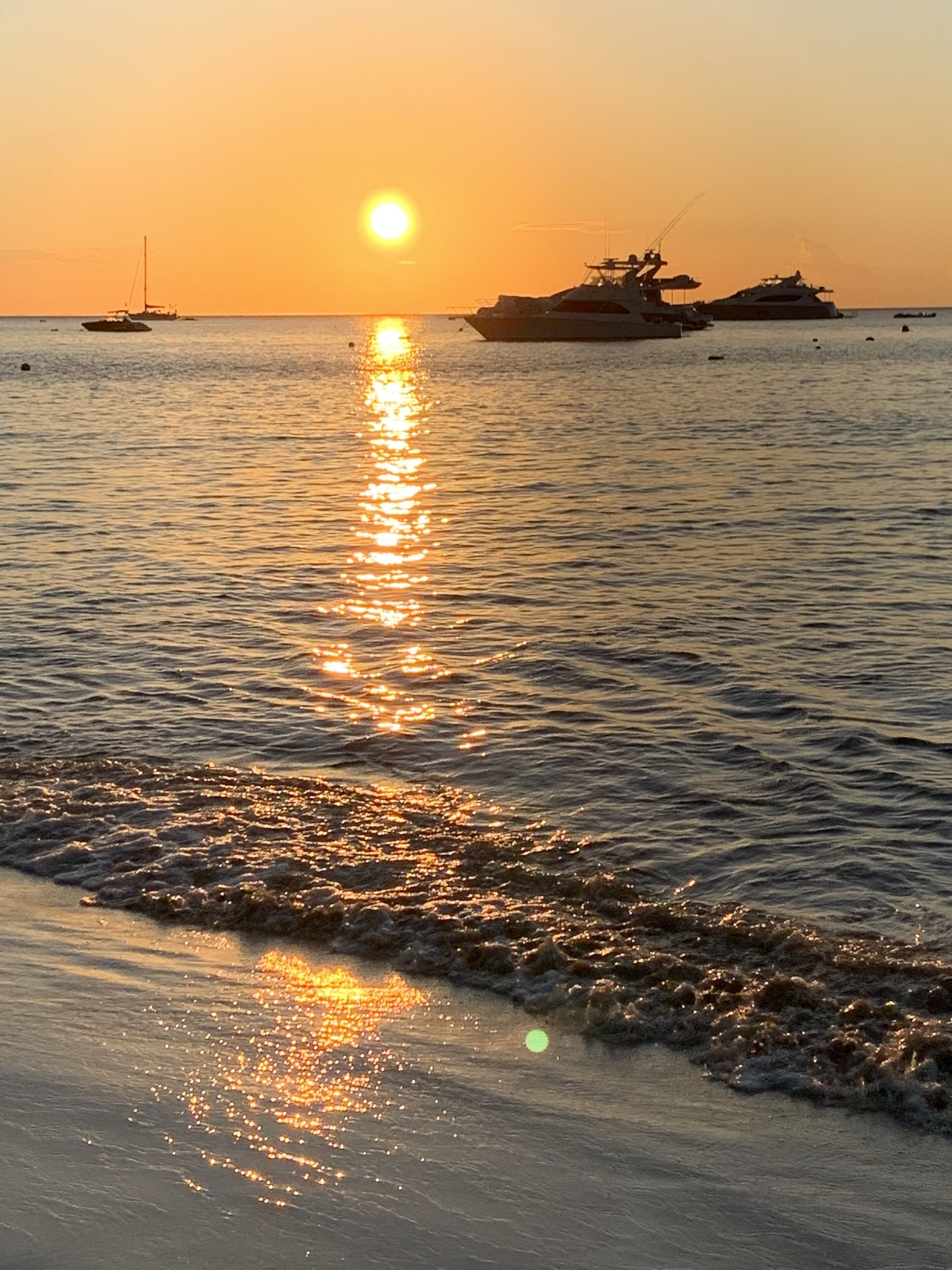Ein Sonnenuntergang über einem ruhigen Meer mit Booten und einem Schiffen im Hintergrund.