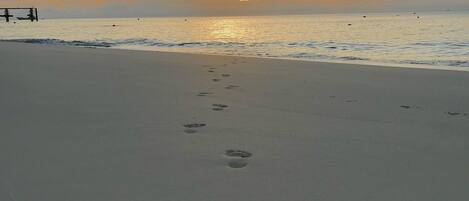 A beach with footprints leading towards the ocean and a sunset in the background.