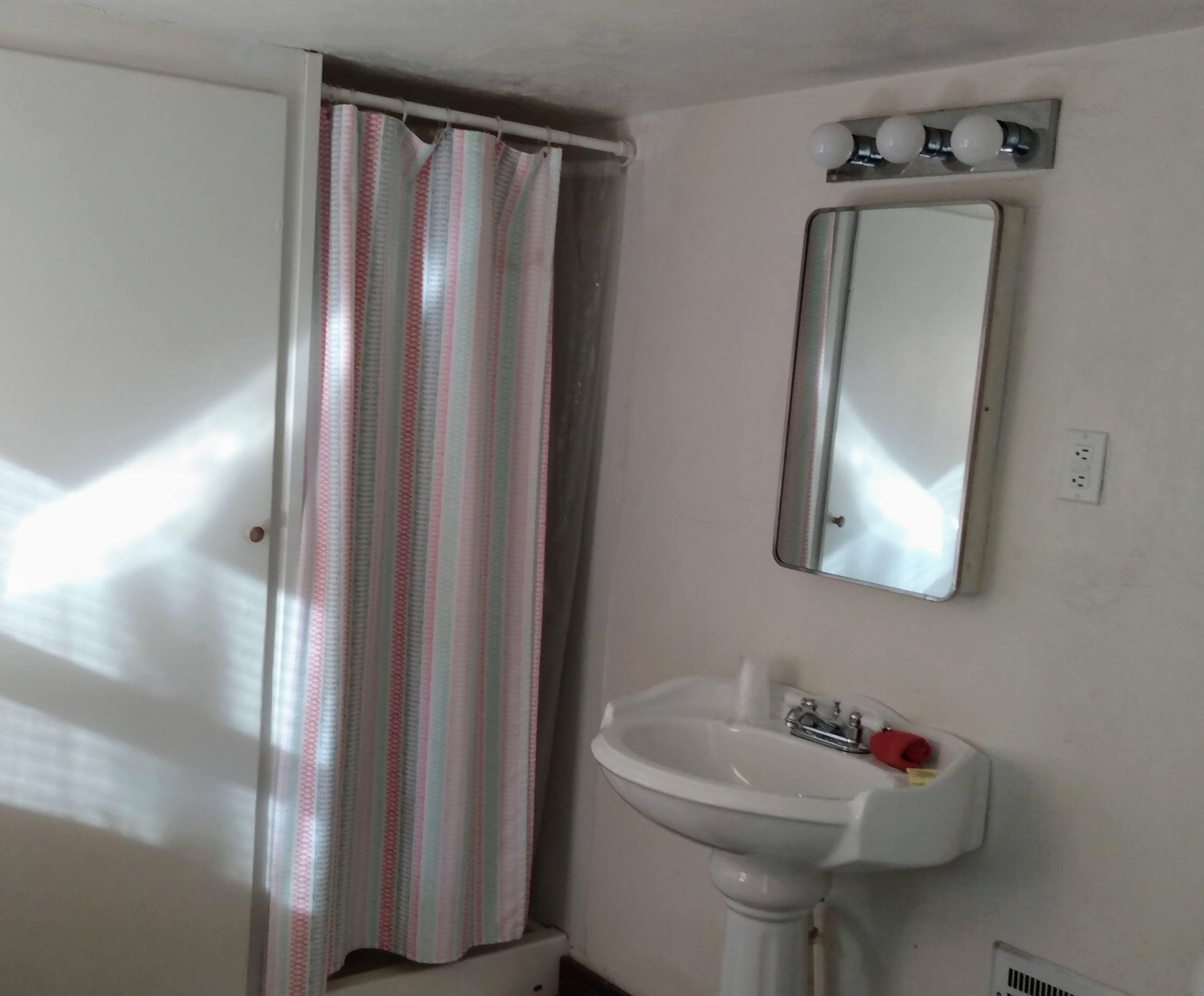 Een badkamer met een gestreepte douchegordijn, een wastafel met een spiegel erboven en een lamp aan de muur.