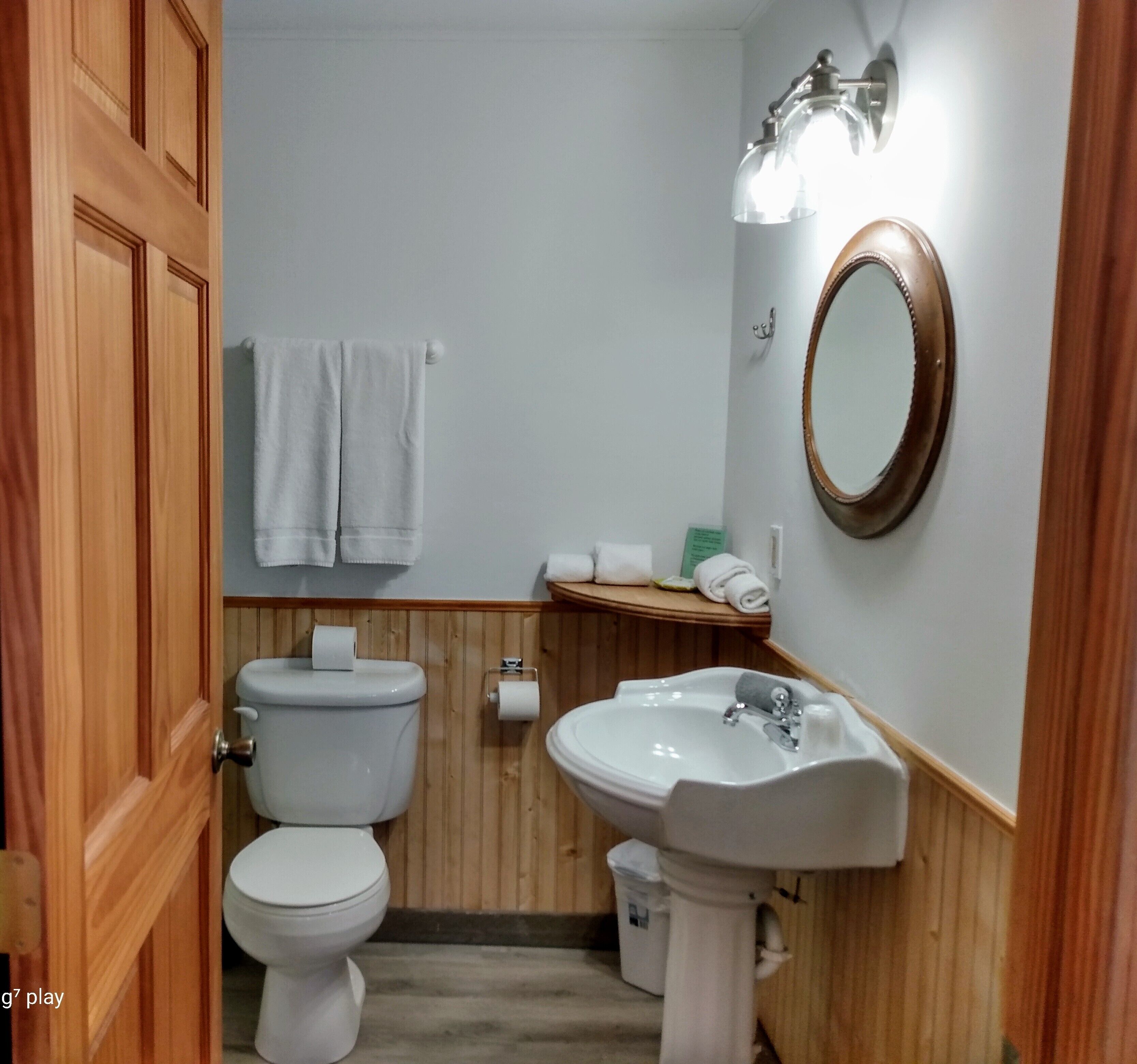 Un baño con inodoro, lavamanos y espejo. Hay toallas colgadas en un perchero y un rollo de papel higiénico en la pared.
