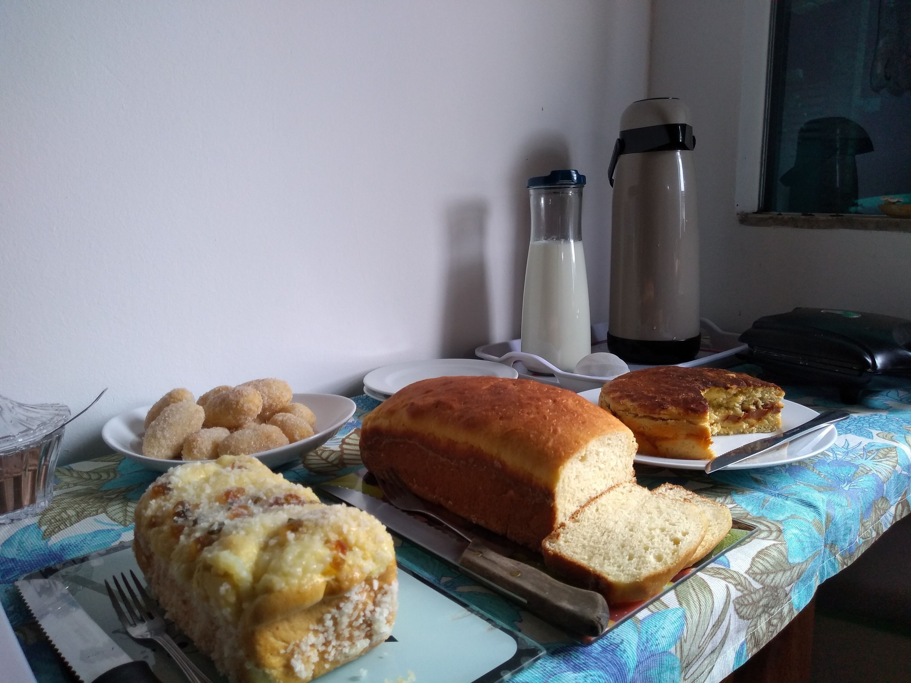 A table with food items including bread and pastries, a milk bottle, a thermos, and a suitcase.