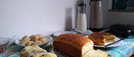 A table with food items including bread and pastries, a milk bottle, a thermos, and a suitcase.