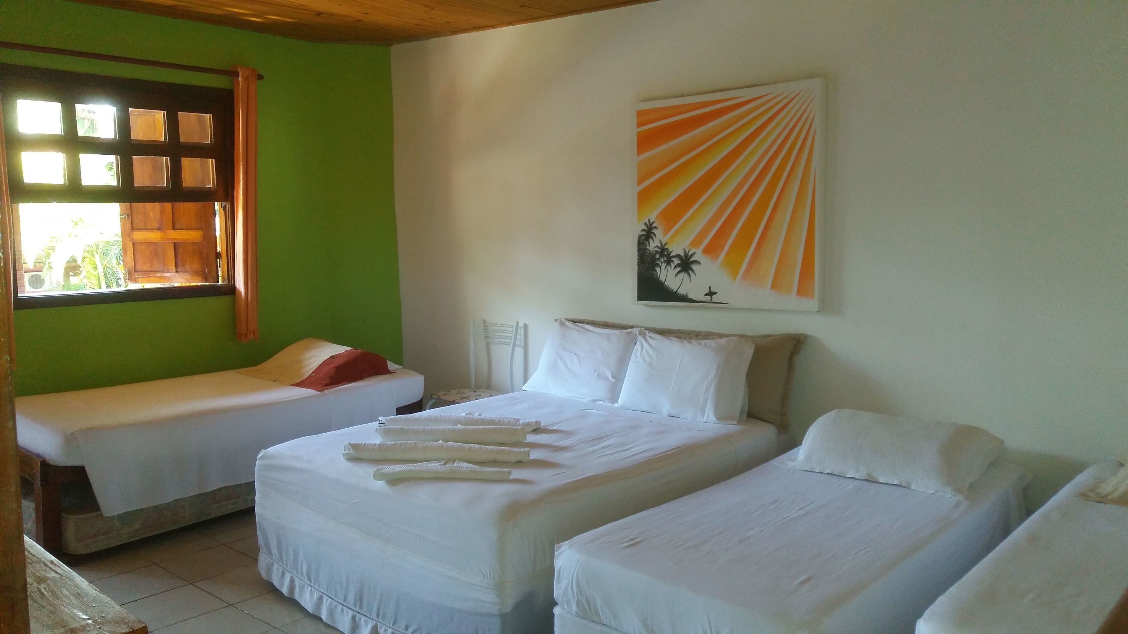 A room with two single beds and one double bed, all with white linens. There is a painting of a sunset on the wall above the double bed.
