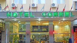 A hotel named HOTEL CORBEL with a modern facade, large windows, and multiple flags displayed above. - Hotel Corbel (Mar del Plata)