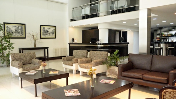 A modern hotel lobby with a reception desk, seating area with patterned sofas, a brown couch, and a bar area. - Hotel Corbel (Mar del Plata)