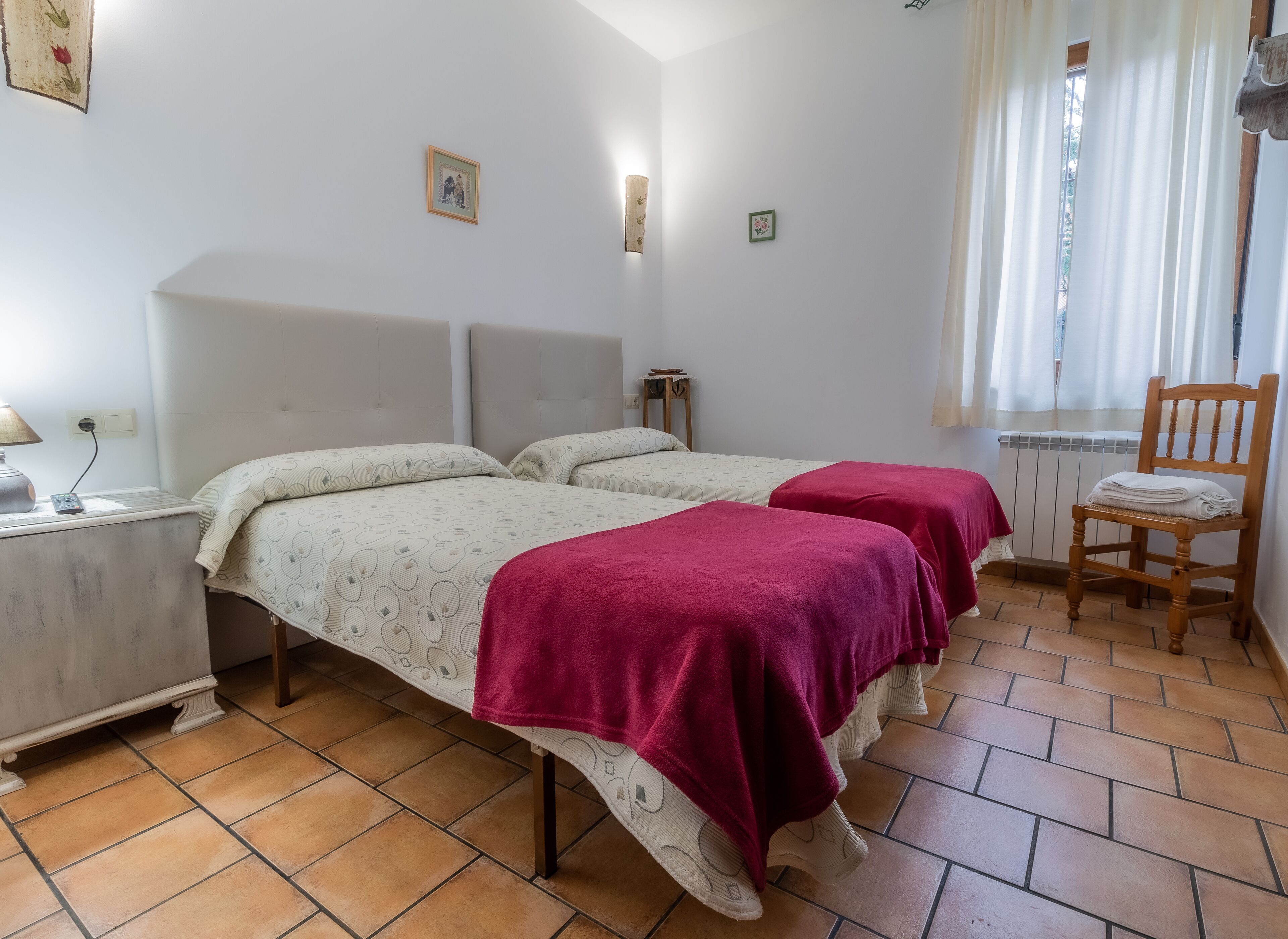 A room with two beds, a chair, a nightstand, and a window with curtains.