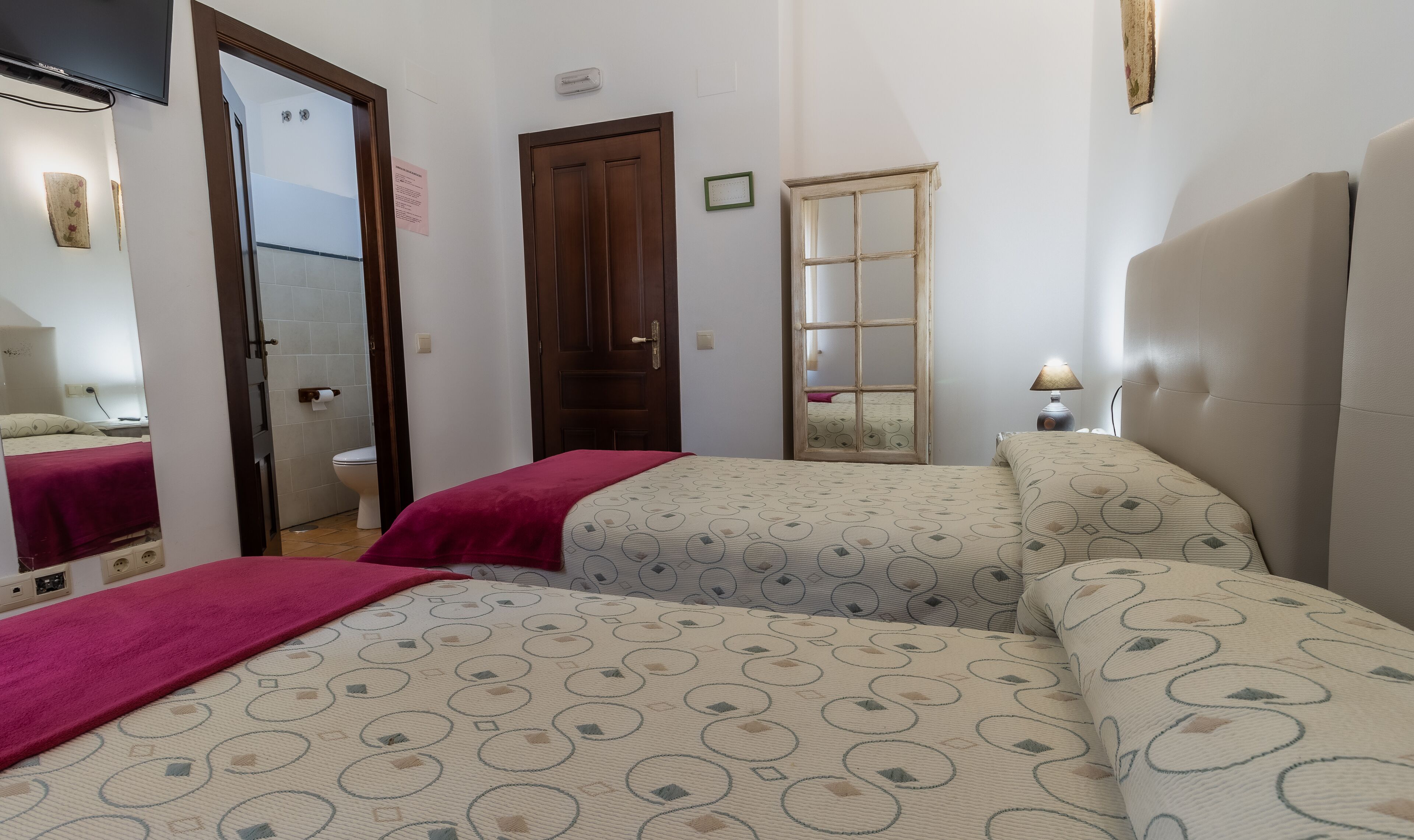 Habitación de hotel con dos camas, una puerta de madera, un espejo y una lámpara de noche.
