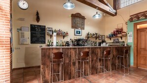 A bar area with a wooden counter, four stools, hanging lights, and a clock on the wall. - Hotel Rural VII Carreras by Vivere Stays (San Pedro de Rozados)
