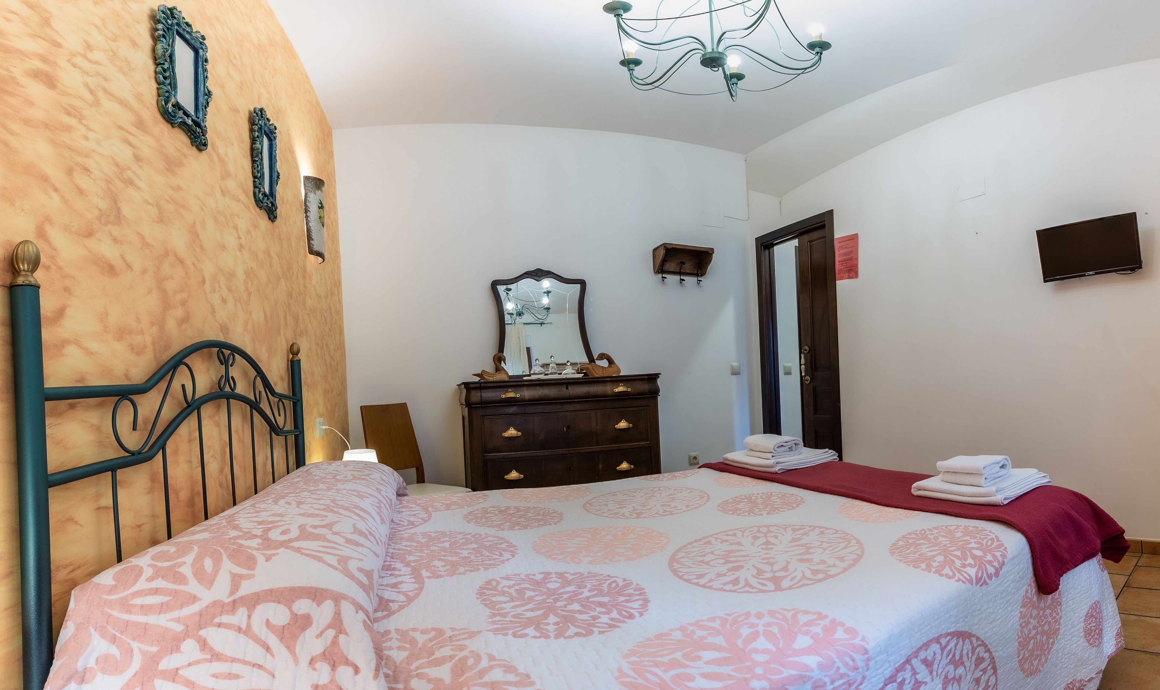 A bedroom with a bed, dresser, mirror, and chandelier.