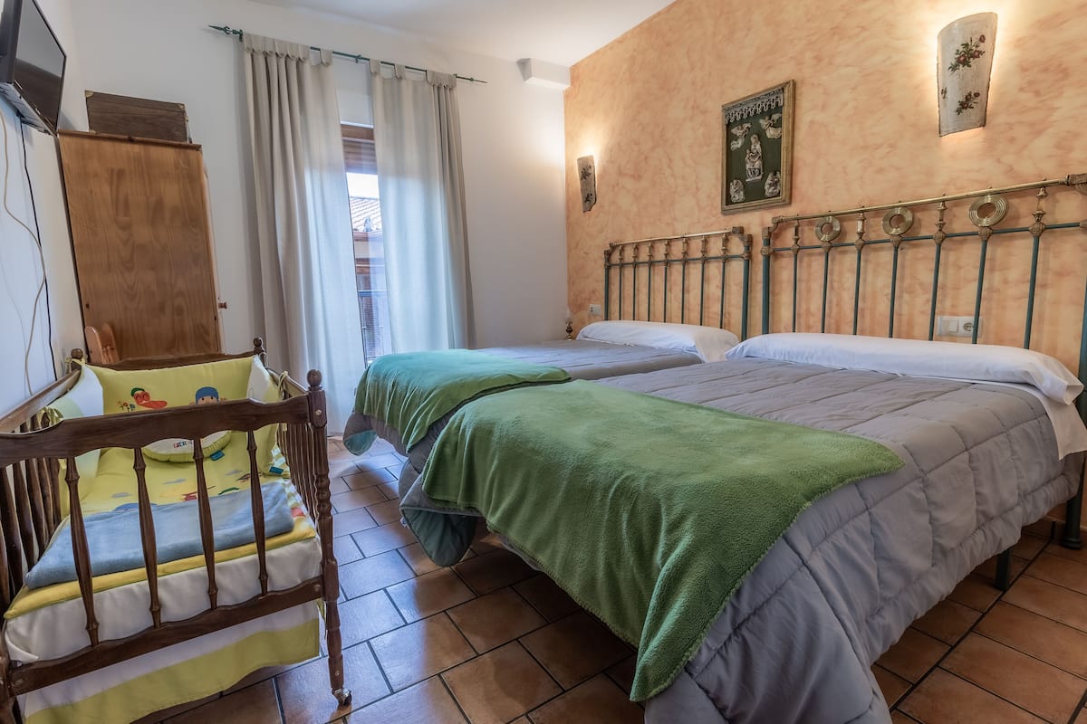 A bedroom with two beds, a wooden crib, and a window with curtains.
